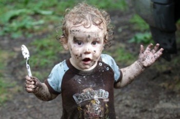 child covered in mud holding a spoon